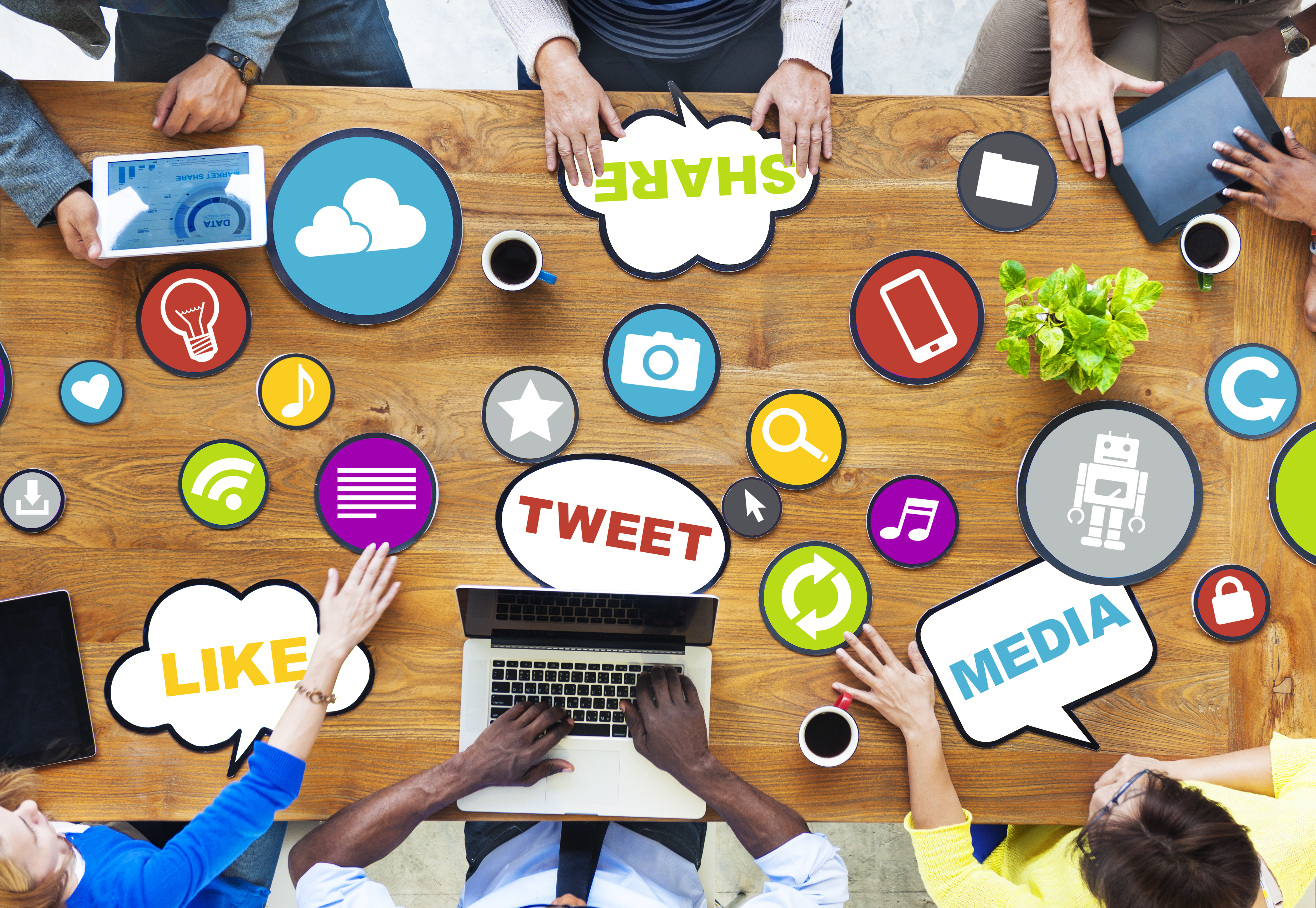 top view of various people's hands holding various colourful social media icons on a meeting table